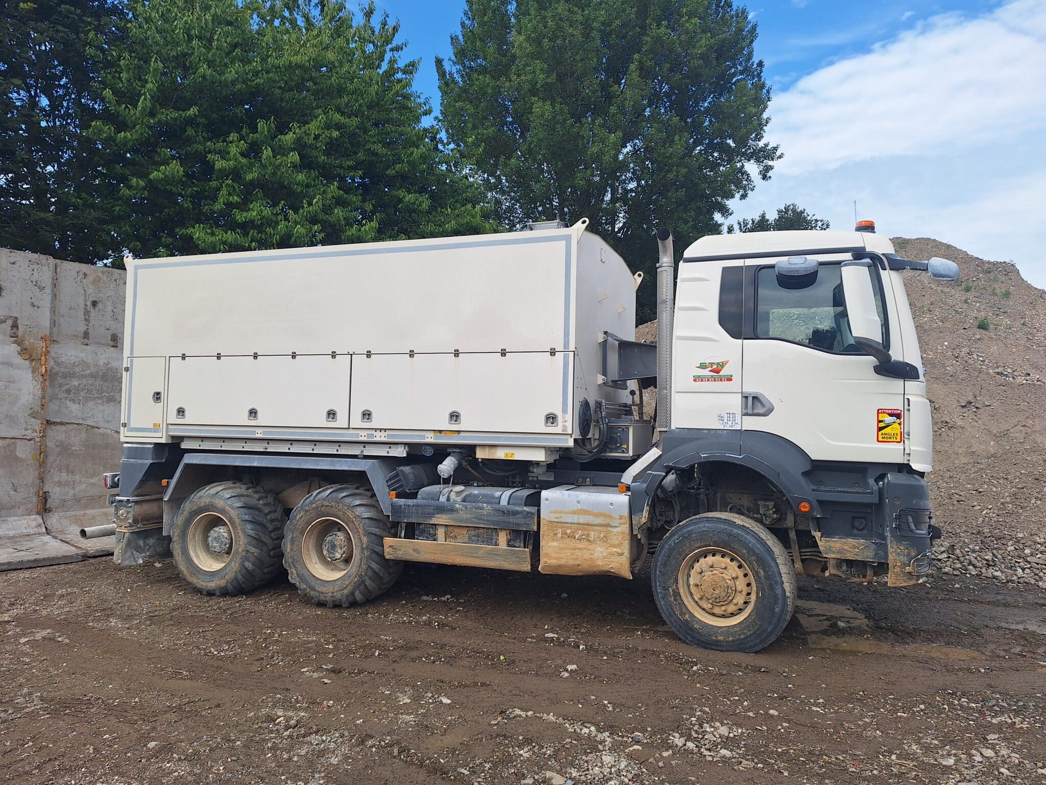 Camion ETN de terrassement blanc sur chantier en terre avec tas de terre autour
